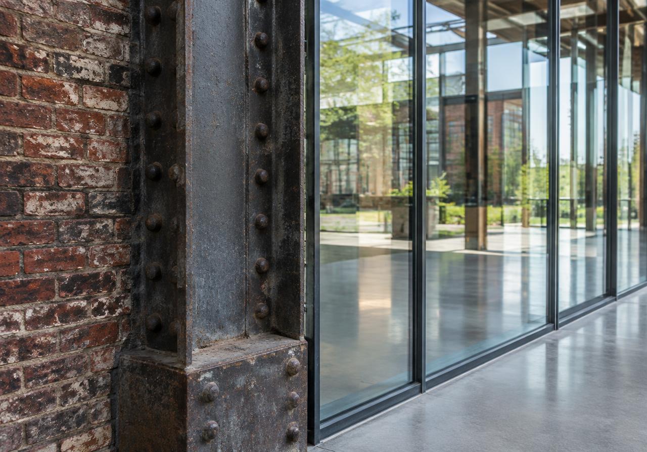 Illustrative image: riveted steel column and old brick meeting a new glass wall